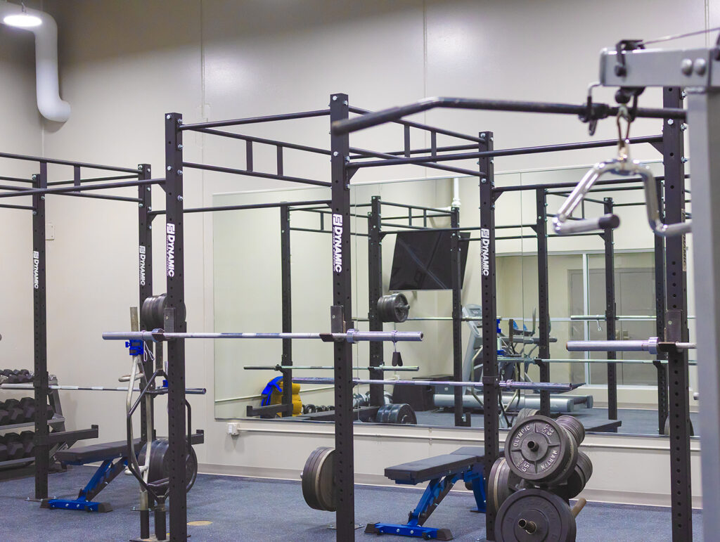 Gym equipment including weight racks, mirrors, and Olympic barbells in a workout space