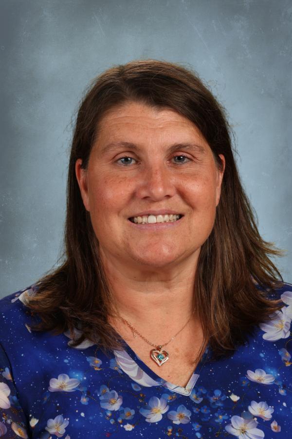 Portrait of a smiling woman with brown hair wearing a blue floral top and a heart necklace.