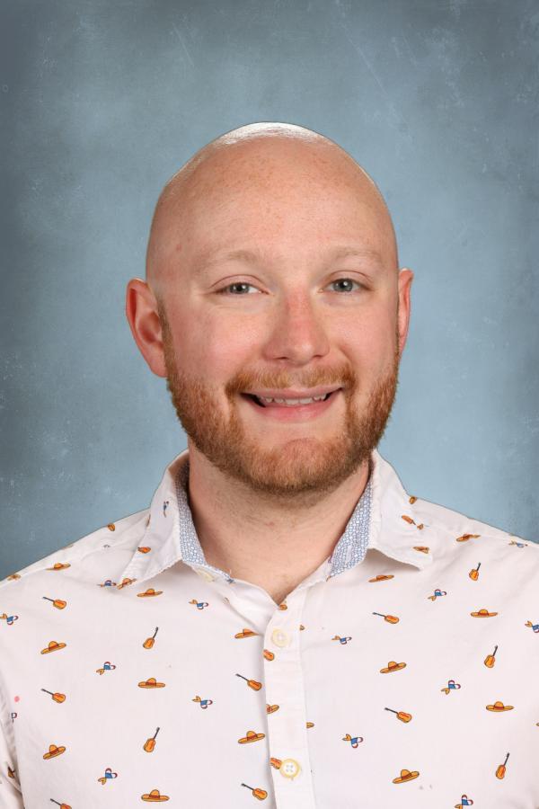 Bald man with beard smiling in a white shirt with colorful patterns