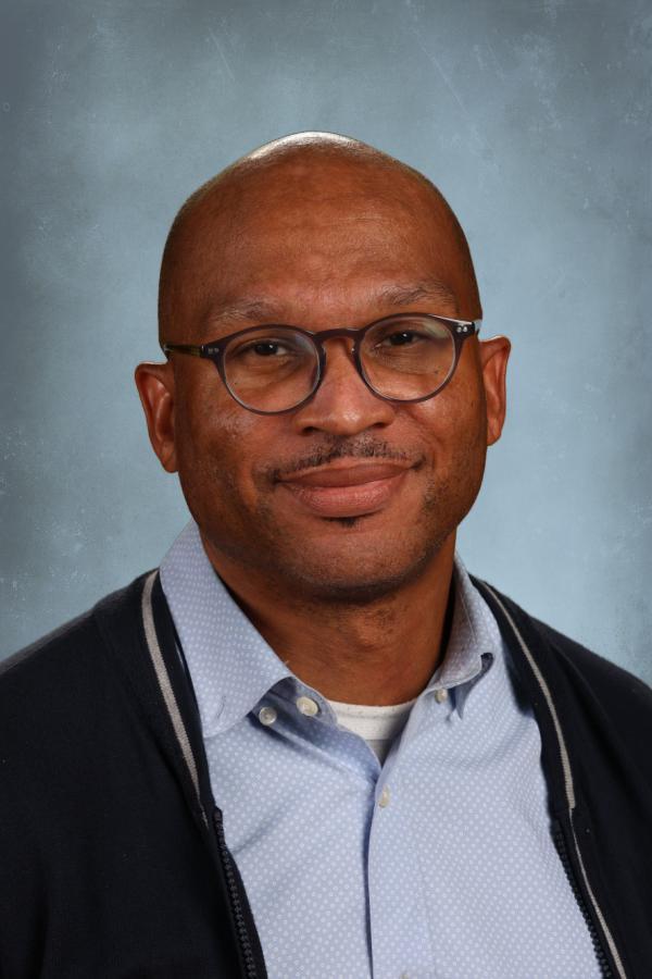 Portrait of a Black man with glasses and a light blue collared shirt.