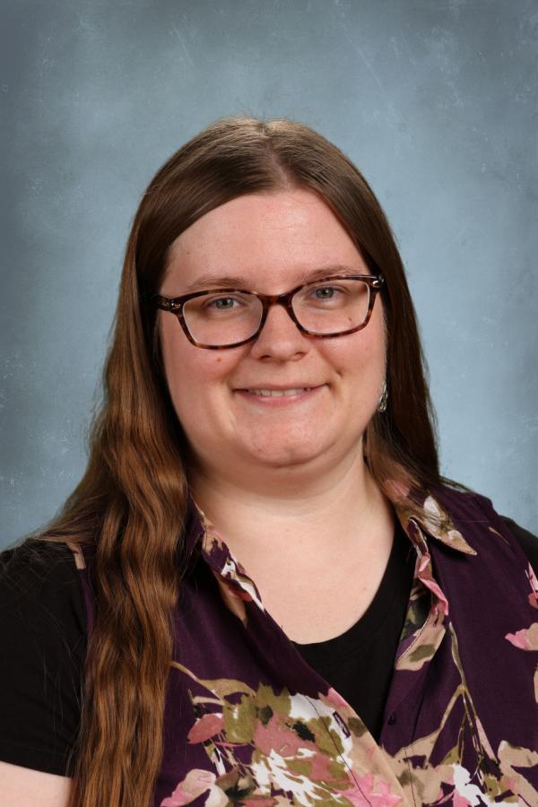 Portrait of a woman with long brown hair and glasses wearing a floral shirt.