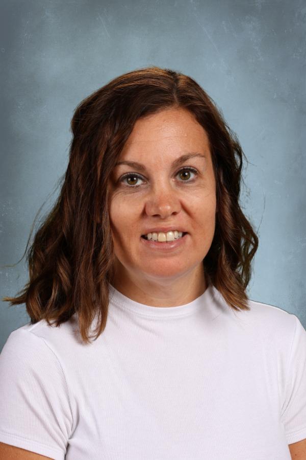 Portrait of a smiling woman with brown hair wearing a white shirt against a blue background.