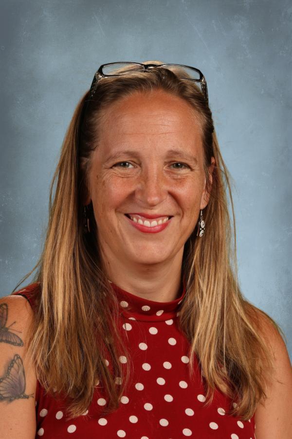 Woman with blonde hair and glasses smiling, wearing a red polka dot top
