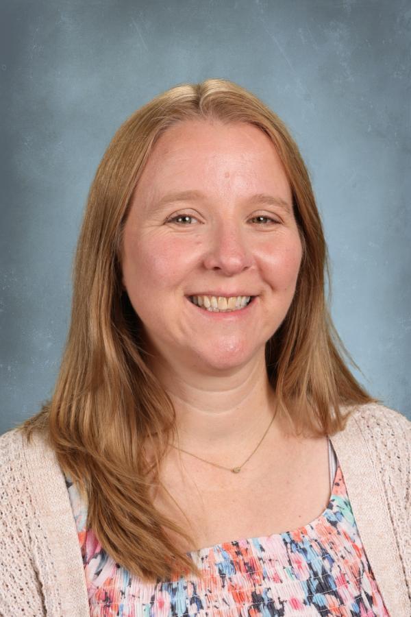 Portrait of a smiling woman with blonde hair wearing a colorful top and a light cardigan.