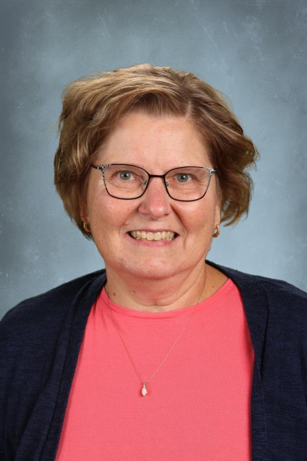 Portrait of a smiling woman with short brown hair, wearing glasses and a coral shirt.