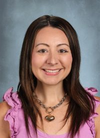 Woman with long brown hair and a heart necklace smiles.