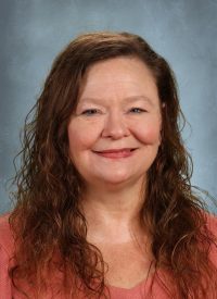 Portrait of a smiling woman with long, wavy brown hair and a coral top.