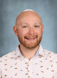 Bald man with beard smiling in a white shirt with colorful patterns