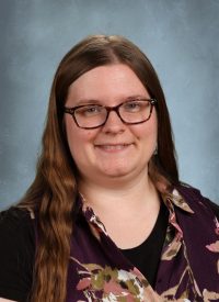 Portrait of a woman with long brown hair and glasses wearing a floral shirt.