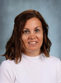 Portrait of a smiling woman with brown hair wearing a white shirt against a blue background.
