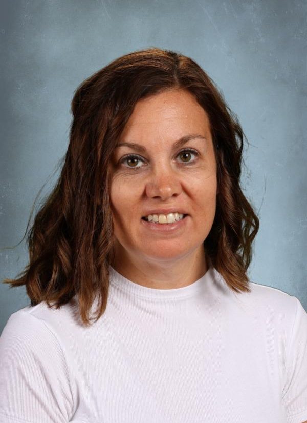Portrait of a smiling woman with brown hair wearing a white shirt against a blue background.