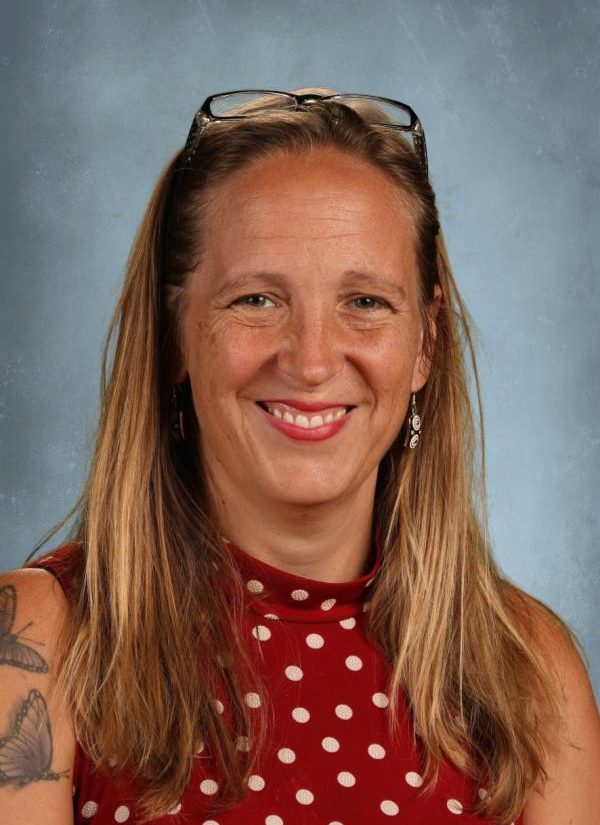 Woman with blonde hair and glasses smiling, wearing a red polka dot top