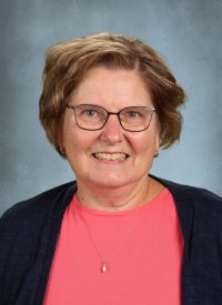 Portrait of a smiling woman with short brown hair, wearing glasses and a coral shirt.